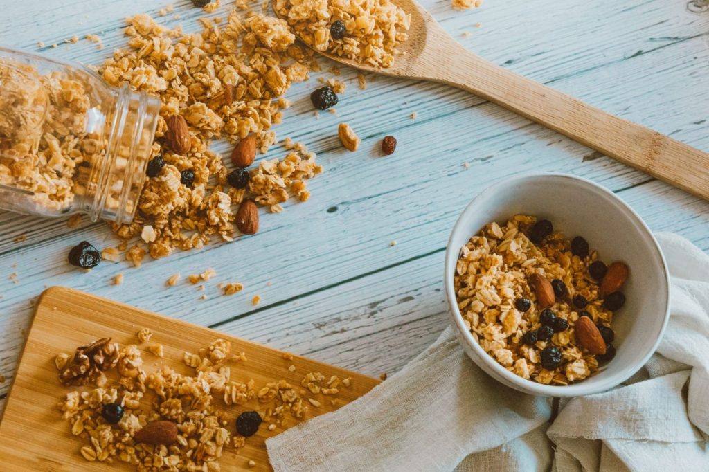 Granola with nuts spilling from a jar onto a wooden board